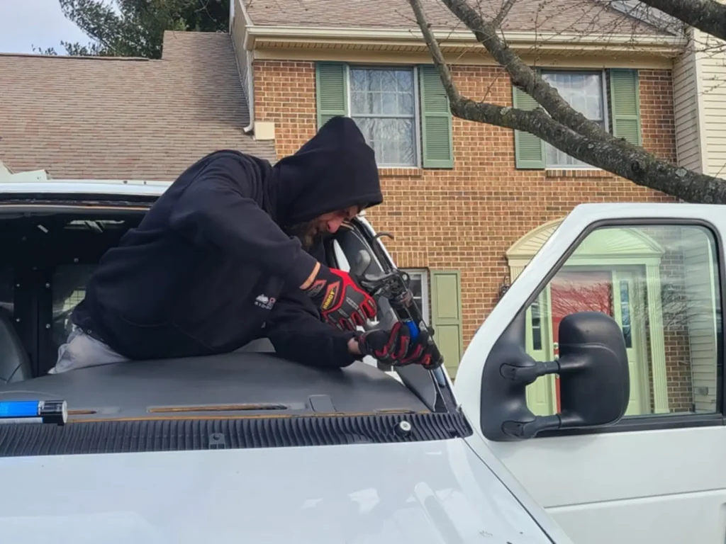 Experienced mobile auto glass technician using specialized tools to remove and replace a damaged windshield on a commercial van at a customer's location.